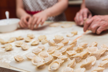 Little girl with grandmother in the kitchen sculpts dumplings