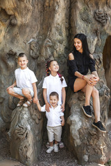 beautiful mother with her three happy joyful cute kids sitting on the tree stem in the park. concept of love and family