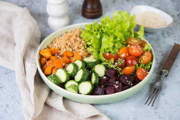 Vegetarian dish a bowl of healthy quinoa with fresh and baked vegetables on a gray concrete background. Close up, selective focuse