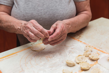 Hands of old woman in the kitchen sculpting dumplings