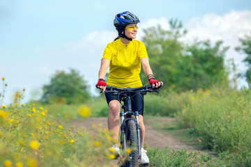 Naklejka na ściany i meble Beautiful girl in yellow riding a bike in nature. Sports and recreation. Hobbies and health.