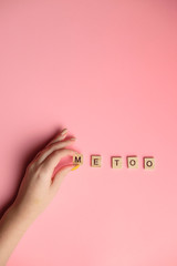 Woman hand making MeToo word with wooden alphabet on pink background, used for concept of sexual harrassment.