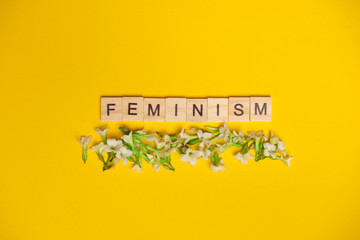 Feminism word on yellow background made of wooden blocks with flowers underneath