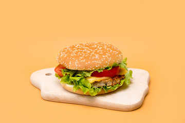 Homemade breaded chicken burger with lettuce on wooden board on yellow background