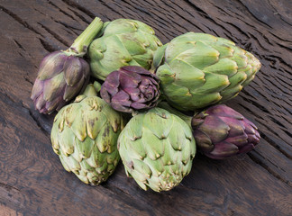 Obraz premium Green and purple artichoke flower edible buds on wooden background.