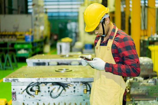 Young engineer in uniform with safety helmet looking at smartphone while upload data or sending text order confirm to customer. Worker Uses Mobile Phone While relax on industry Manufacturing Factory