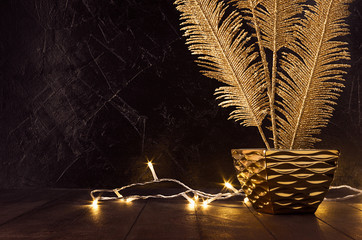 Luxury home accessories in black and gold color - warm glowing lights and golden glittering branch in bowl on dark  wood table with black plaster wall.