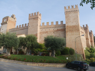 External walls with towers and laces around the village of Gradara with olive trees and green lawn.