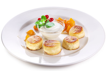 Cheese cakes with sour cream, slices of sweet peach, mint and red currants on a white plate. Clipping path.