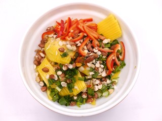 Top view photo of a large white bowl with salad ingredients - sliced mango. bell pepper, green onions / scallions. chopped peanuts. Healthy salad photo.