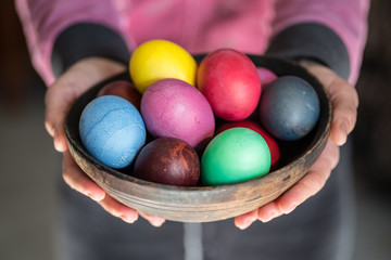 Colorful Easter eggs in bowl in woman's hands.