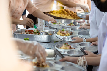 Asian teachers are distributing food to students,elementary school students are wait or queuing to receive free food,children during lunch break,eating lunch or school activity,back to school concept