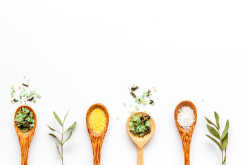 Colorful spa salt in spoons - with herbs - on white background top-down frame copy space