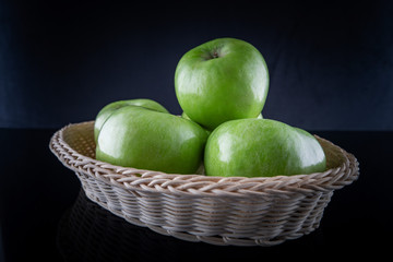 Green apples in a basket with reflection, on a black background, shallow depth of field. Concept, healthy eating, lifestyle.