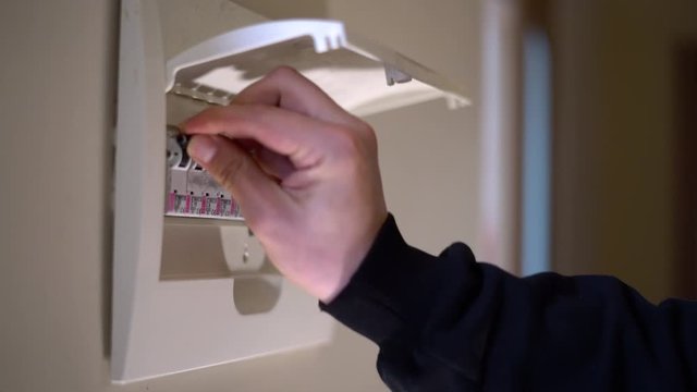 Hand switching power switch on a fusebox. Close up of electrician checking fuse box knob