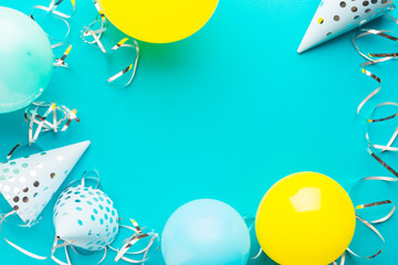 Blue caps, blue and yellow balloons and silver serpentine on a blue paper background. Holiday background. Copy space
