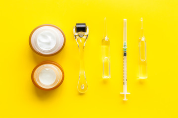 Dermatologist work desk with tools. Dermaroller, syringe, ampoule on yellow background top-down flat lay