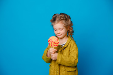 portrait of a baby girl in a coat holding a Lollipop on a colored blue background