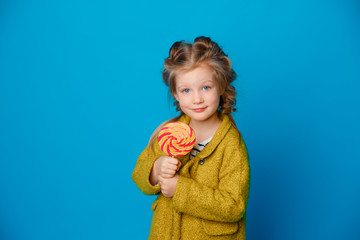 portrait of a baby girl in a coat holding a Lollipop on a colored blue background