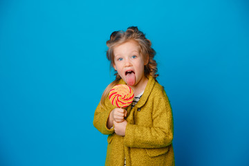 portrait of a baby girl in a coat holding a Lollipop on a colored blue background