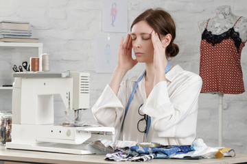 Sleepy, frustrated, exhausted seamstress with headache on her work desk. Small business or...