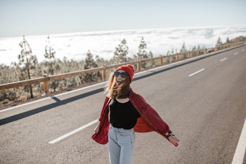 Portrait of a cheerful woman stylishly dressed in red shirt and hat, feeling free and joyful on the road above the clouds. Carefree lifestyle and travel concept