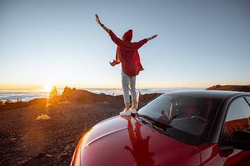 Young woman rocky landscapes above the clouds, standing on the car highly in the mountains. Carefree lifestyle and travel concept