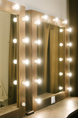 Luminous bulbs are arranged in a row vertically on the surface of the mirror, near the makeup table. Illumination of a mirror in a bathroom, copyspace