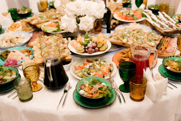 The round white table is filled with a large amount of food and various snacks in a luxurious interior, beautiful serving of the holiday table