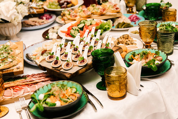 The round white table is filled with a large amount of food and various snacks in a luxurious interior, table setting, selective focus