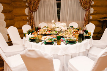 The round white table is filled with a large amount of food and various snacks in a luxurious interior, beautiful serving of the holiday table
