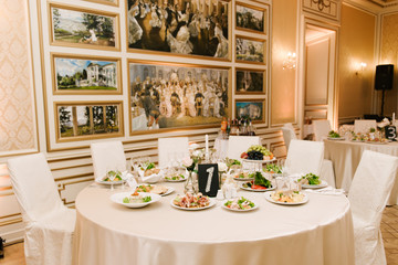 The round white table is filled with a large amount of food and various snacks in a luxurious interior, beautiful serving of the holiday table