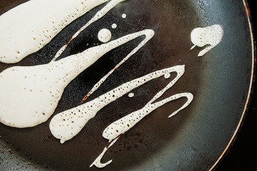 batter with bubbles is fried in a black pan with a rusty handle with drops of fat and oil on an...