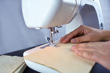 Close up view of sewing process. Female hands stitching  on professional manufacturing machine at...