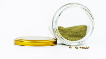 Close-up of glass jar with hashish and cannabis seeds isolated on white background.