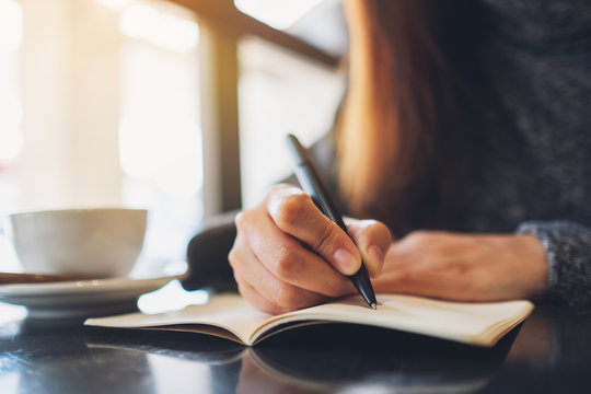 Closeup image of a woman writing on a blank notebook on the table