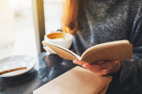 Closeup image of a woman reading a book while drinking coffee in the morning