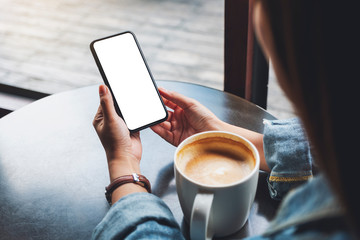 Mockup image of a woman holding black mobile phone with blank white screen with coffee cup on the table - Powered by Adobe