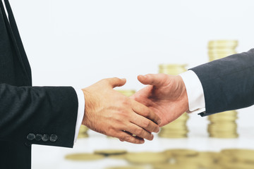 Handshake of two businessmen on the background of growing stacks of golden coins, investing concept, close up
