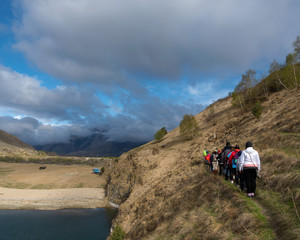 Obraz premium Bylym village, Kabardino-Balkarian Rep, Russia, 03/03/2019 a group of tourists walking along a trail next to a lake surrounded by mountains.