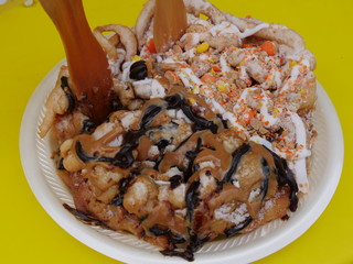Close up of a chocolate-flavored and caramel-flavored funnel cake on a styrofoam plate.
