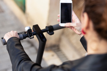 Woman riding his electric scooter and looking at mobile phone.