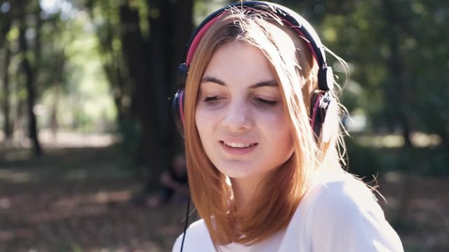 Portrait of pretty positive teenage girl with red hair listening to music in pink earphones smiling happily.