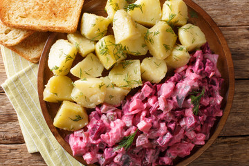herring salad with beets, onions, apples, pickled with a side dish of boiled potatoes close-up in a plate. Horizontal top view