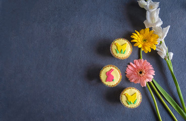 Pretty yellow vegan Easter cupcakes with colorful pastel icing shapes of Easter bunny rabbits, chicks together with Easter flowers