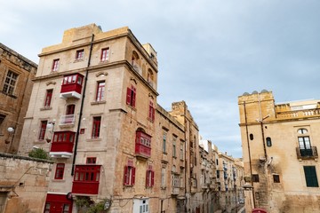 Fototapeta na wymiar The very old houses with red windows and balconies at Liesse street in Valletta, Malta