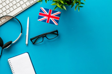 Learn English online. Concept with british flag, headset and keyboard on blue background top-down copy space