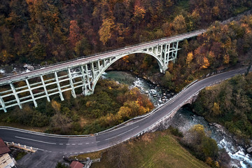 high autumn alpine speed road in Italian Alps and railway bridge over the mountain river.