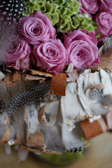 Beautiful spring bouquet close-up with pink roses and green carnations, decorated with feathers and birch bark. 