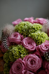 Beautiful spring bouquet close-up with pink roses and green carnations, decorated with feathers and birch bark. 
